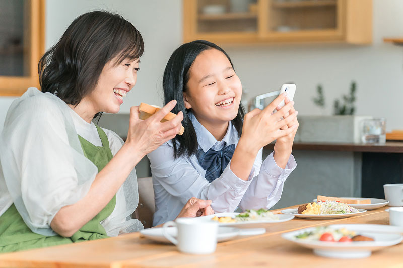 スマートフォンを見ながら笑顔で話す親子の様子